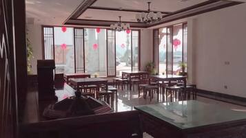 A spacious dining area with multiple tables and chairs, large windows with red decorations, and a modern ceiling design.