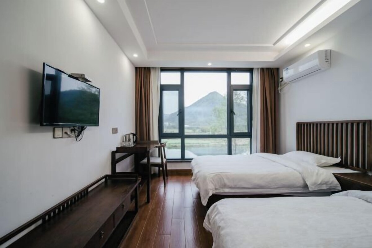 Ein Hotelzimmer mit zwei Betten, einem an der Wand befestigten Fernseher, einem Schreibtisch und einem Fenster mit Blick auf die Berge.