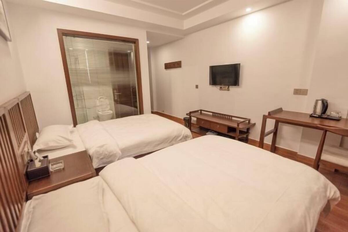 Hotellihuone, jossa on kaksi sänkyä, televisio, työpöytä ja pieni pöytä.