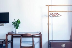 A room with a wooden desk, a chair, a potted plant, a TV mounted on the wall, and a clothing rack. - Wuyuan Qingyun Hotel (Wuyuan)