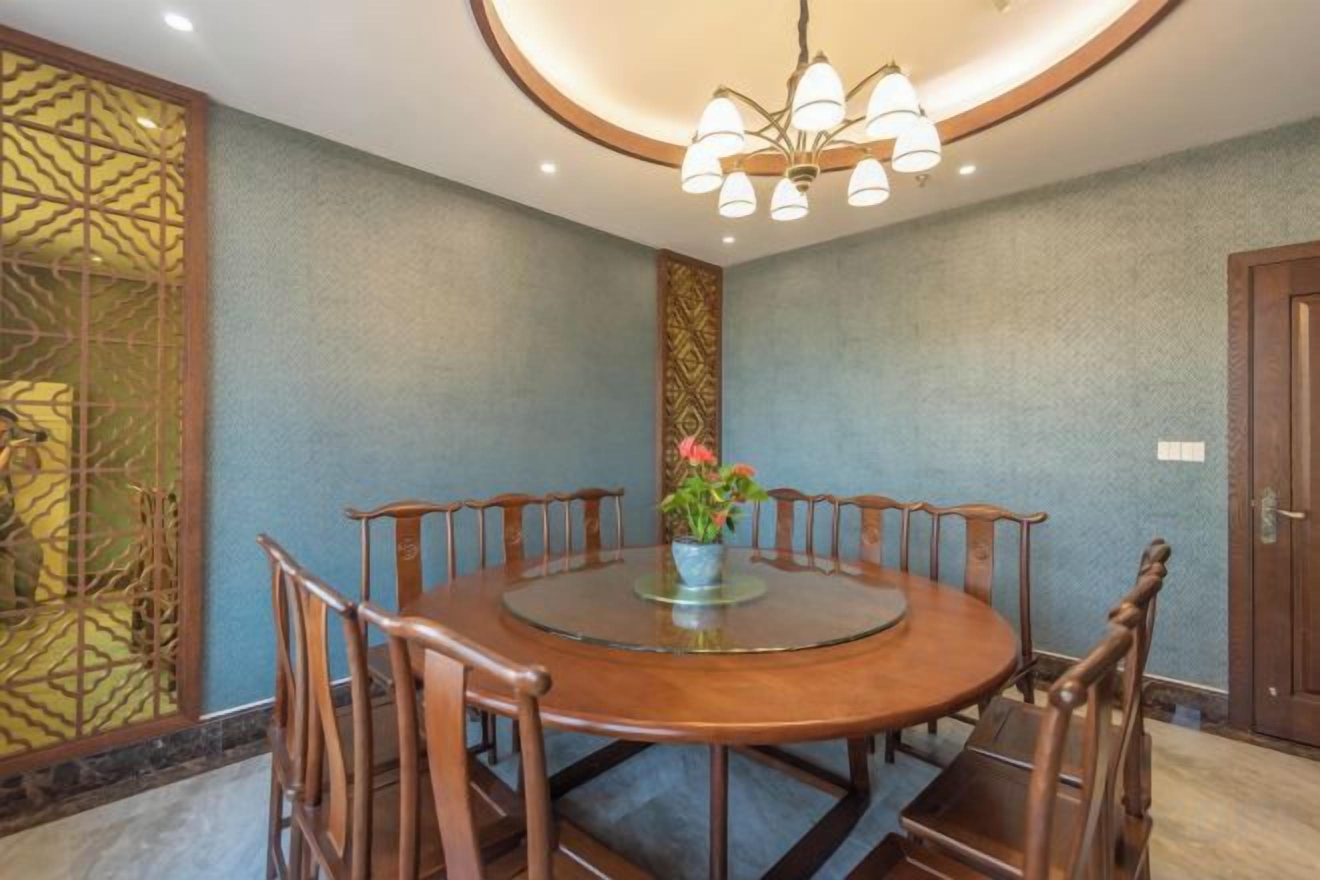 Une table de salle à manger ronde, avec des chaises, un lustre et un panneau décoratif mural.