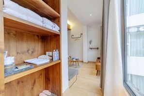 A hotel room with wooden shelves, a bed, a small table with a chair, and a window with curtains. - Amila Guesthouse (Dali City)