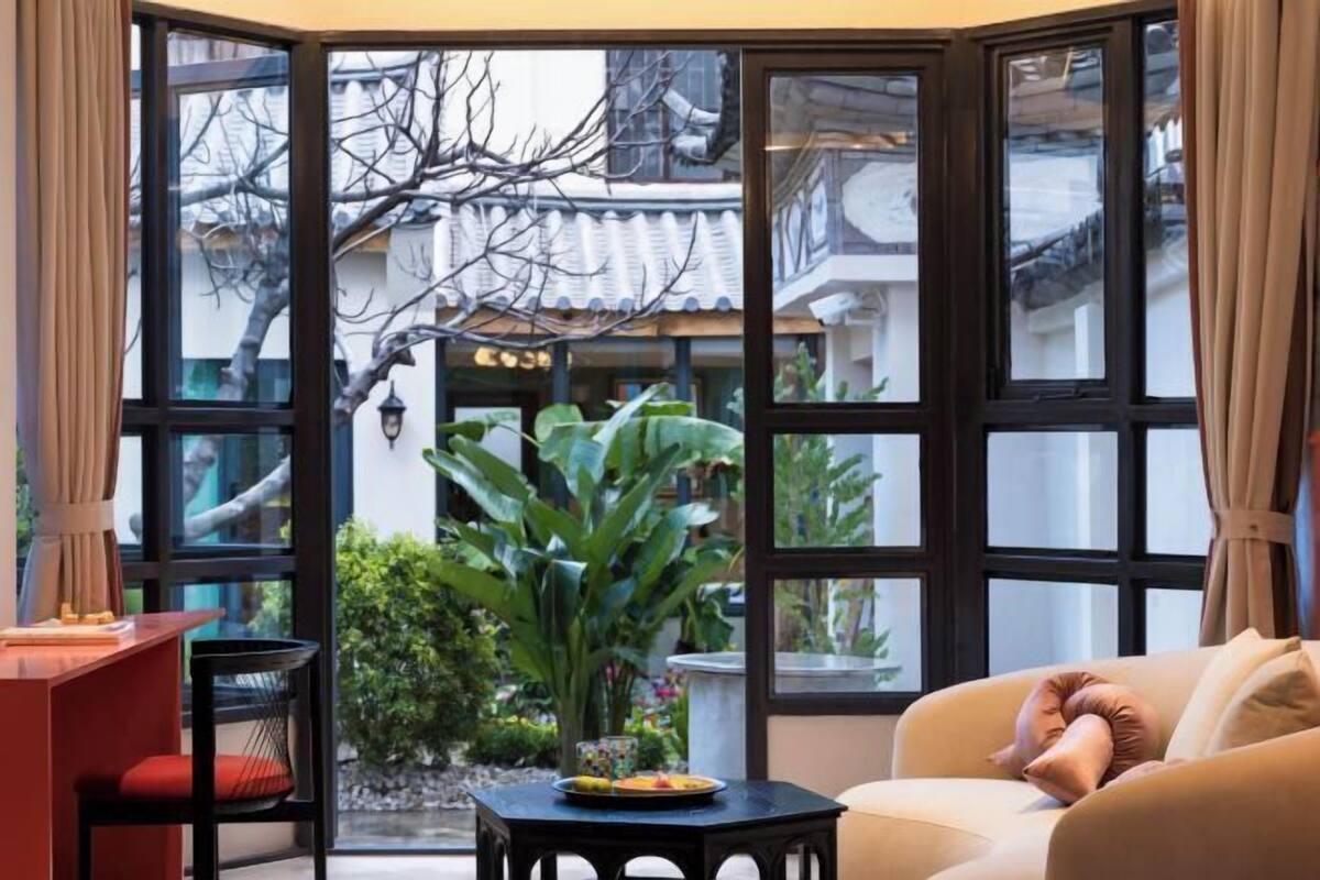A room with a large window, a sofa, a small table with a plant, and a chair.