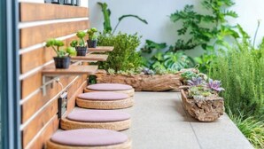 A wooden bench with cushions, potted plants, and a concrete pathway. - Amila Guesthouse (Dali City)