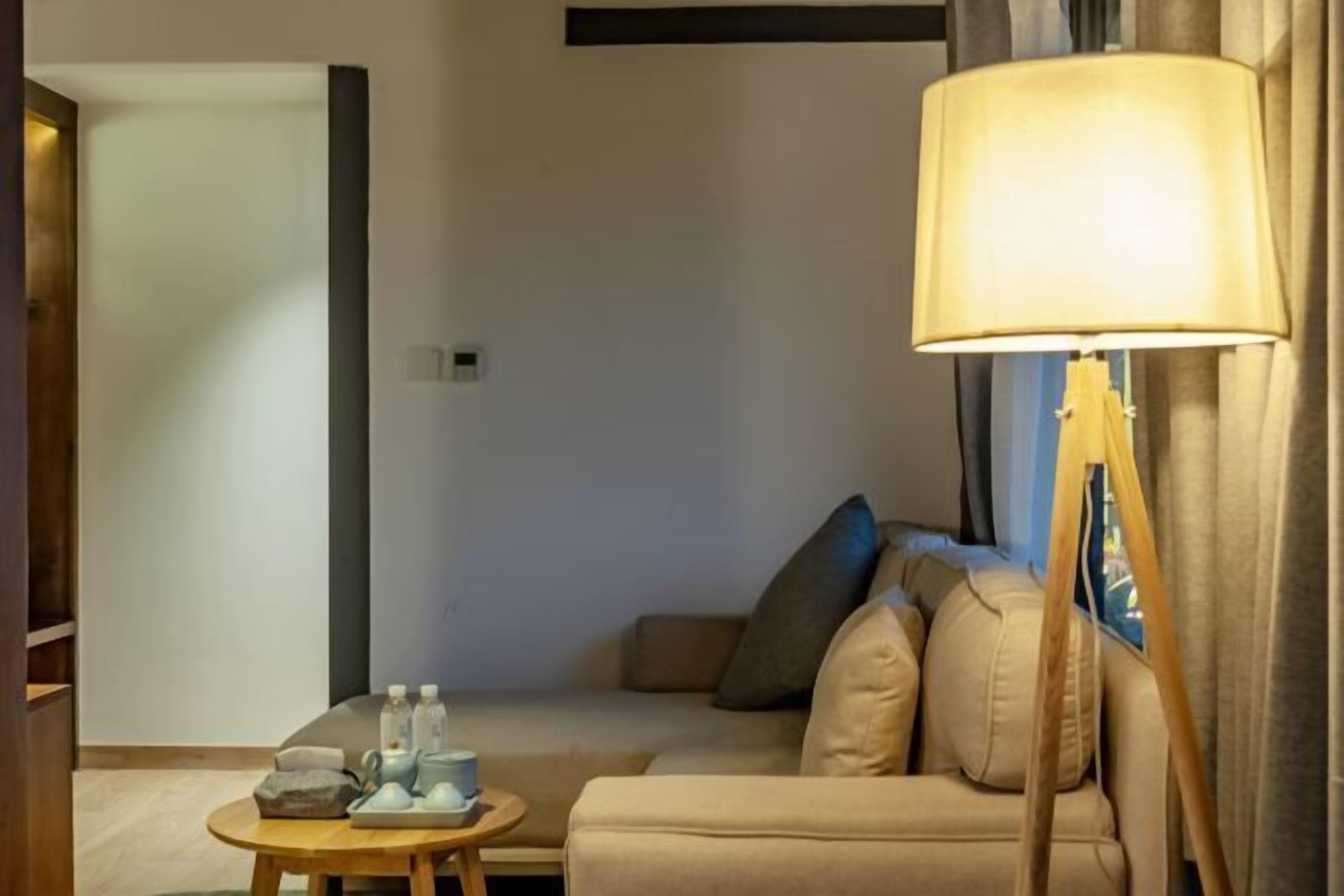 A cozy living room with a beige sofa, a round wooden coffee table, and a floor lamp.