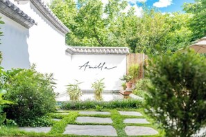 Een tuinpad dat leidt naar een wit gebouw met een bord waarop 'Amilla' staat.