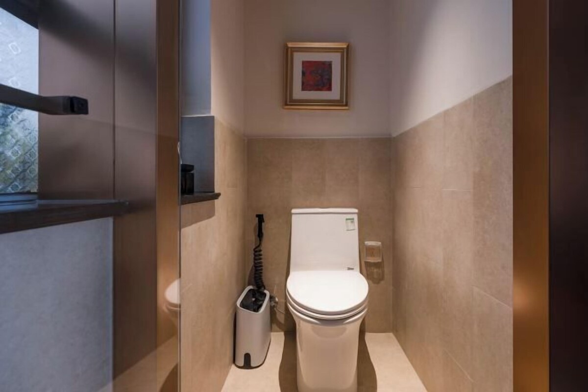 A compact bathroom with a toilet, a trash bin, and a framed picture on the wall.