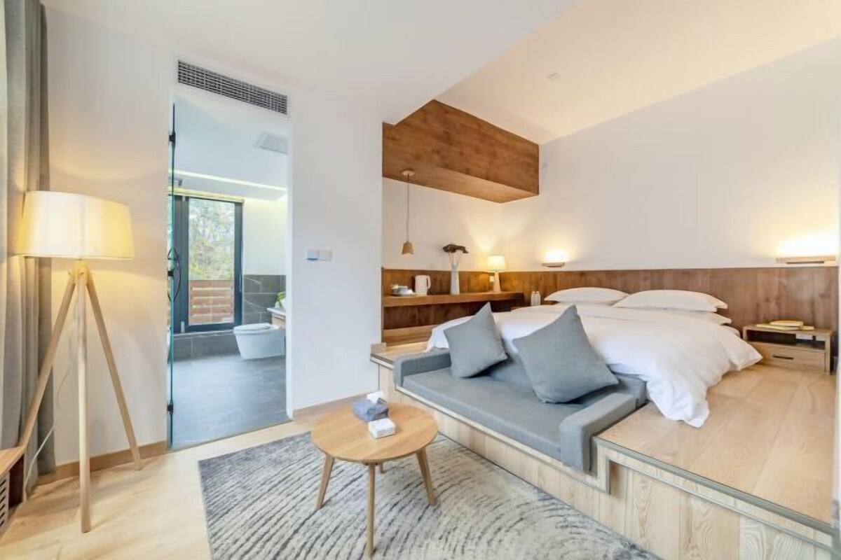 A modern hotel room with a sofa bed, bedside tables, a lamp, and a view of the outdoors.