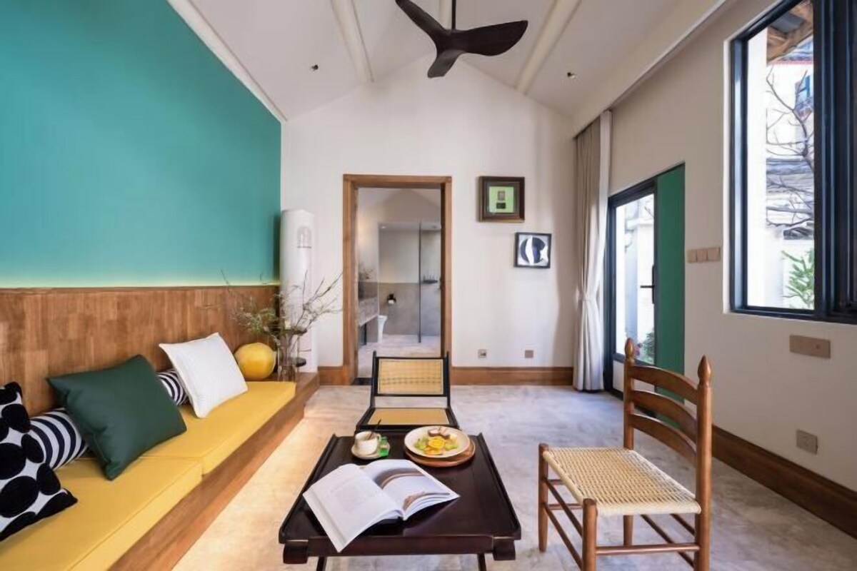 A modern living room with a sofa, a dining table with a book, a chair, and a ceiling fan.