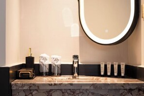 A bathroom with a marble sink, a round mirror with a light, and toiletries. - Amila Guesthouse (Dali City)