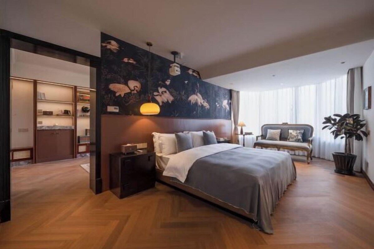 A modern bedroom with a large bed, a nightstand, a sofa, and a wall with a floral mural.