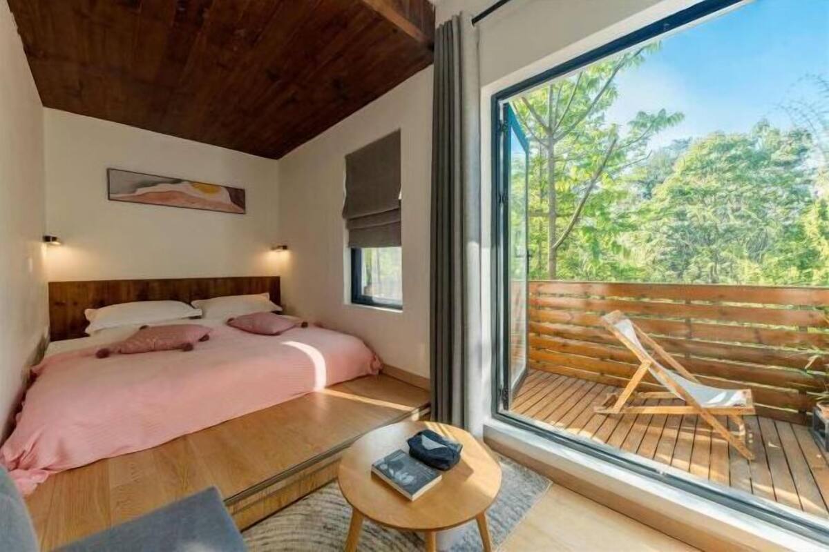 A bedroom with a large bed, a small table, and a view of a wooden deck outside.