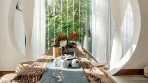 A room with a long table set for tea, a wooden bench, and a view of greenery through sheer curtains. - Amila Guesthouse (Dali City)