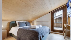 A bedroom with a sloped ceiling, a bed with a dark headboard, a window with a view, and a wooden floor. - New rooftop with south balcony, parking and wifi (Montvalezan-La Rosière)