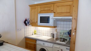 Eine kompakte Küche mit Holzausstattung, einer Mikrowelle, einer Waschmaschine und einem Spülbecken.