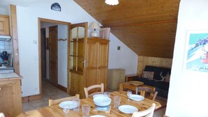 Ein Essbereich mit Holztisch, gedeckt für vier Personen, eine Küchenzeile mit Kühlschrank und ein Wohnzimmer mit Sofa und einem Bild an der Wand.