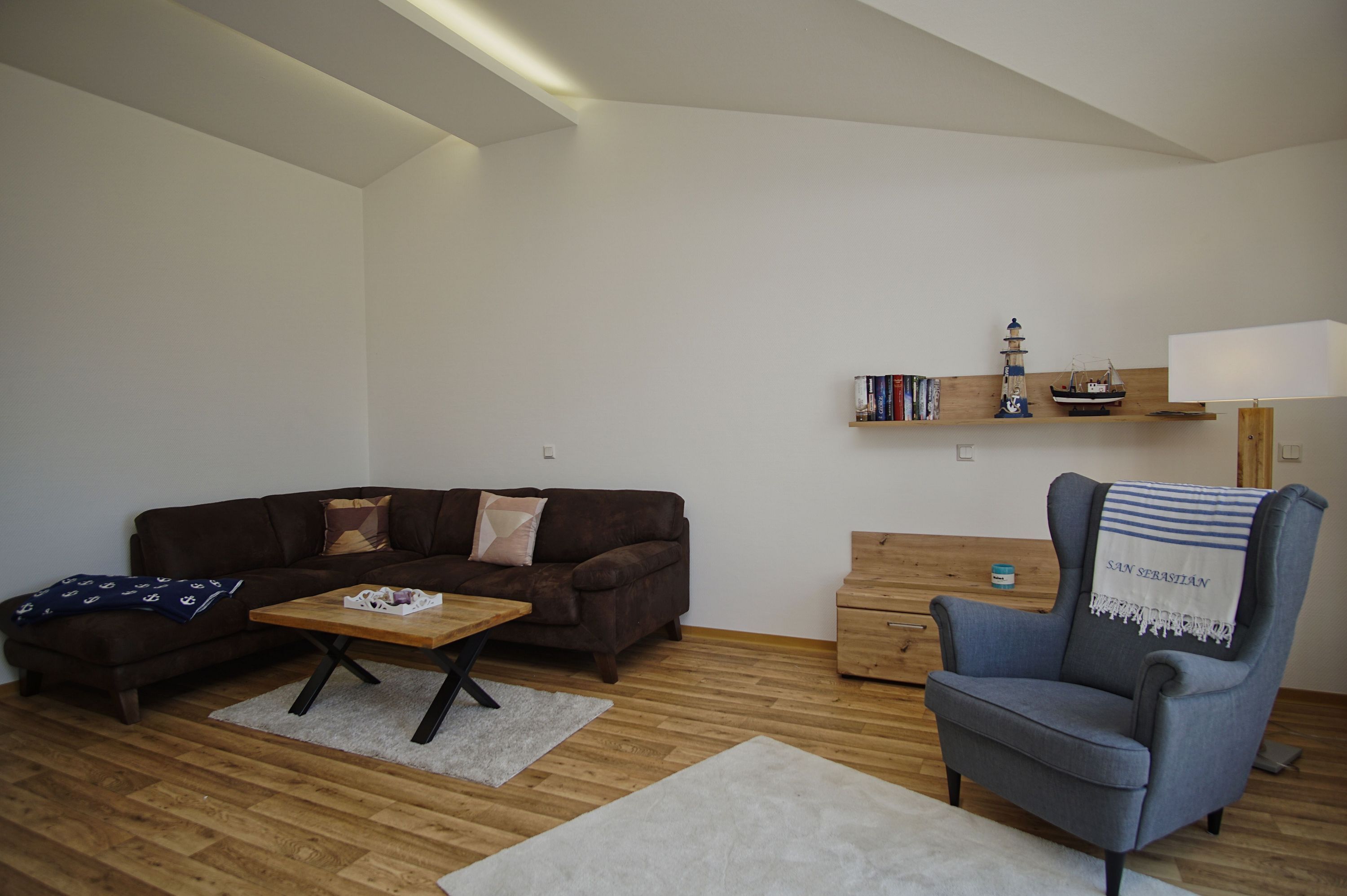 A living room with a brown sofa, a wooden coffee table, a blue armchair, and a bookshelf with books and decorative items.