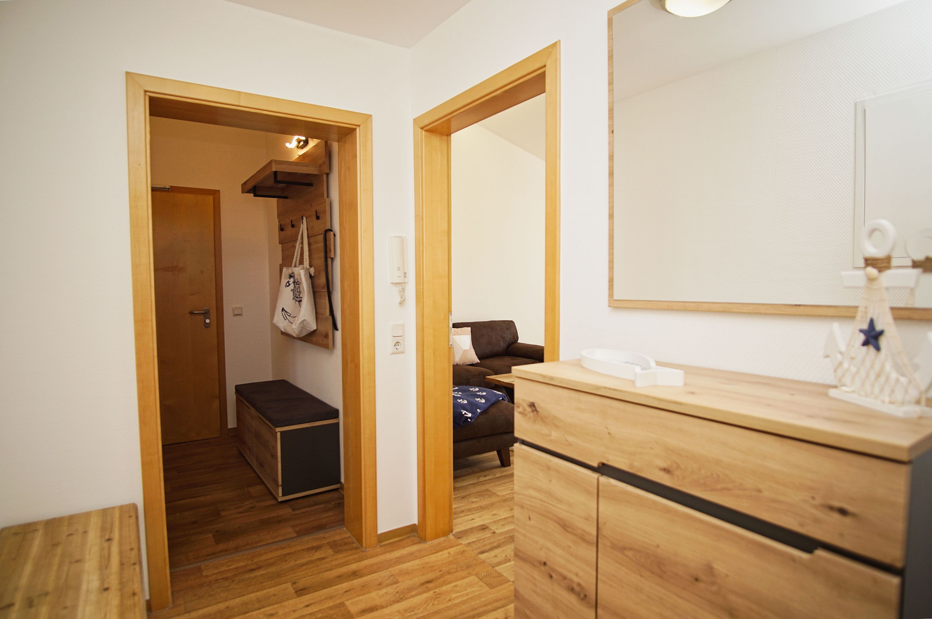 A compact room with wooden flooring, a bench, a wardrobe, a mirror, and a small table with a decorative item.