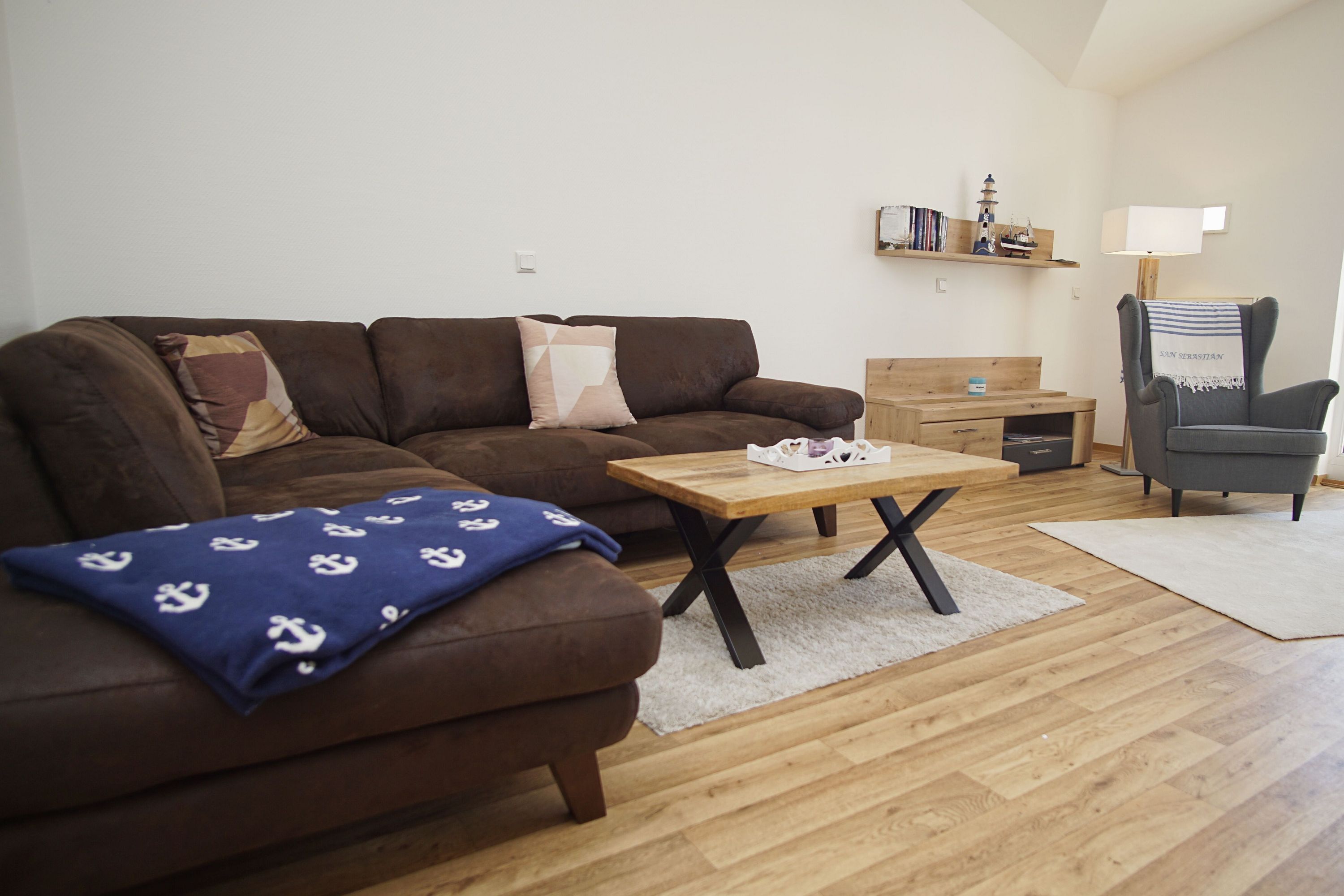 Een woonkamer met een bruine bank, een houten salontafel, een grijze fauteuil en een klein houten kastje.