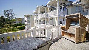 A wooden deck with a table and chairs, a wicker sofa, and a white railing. - With sea view and balcony, use of swimming pool and sauna - Sea view apartment 51 (Göhren (Ostseebad))