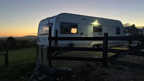 Een caravan geparkeerd in de schemering, met een houten hek op de voorgrond.