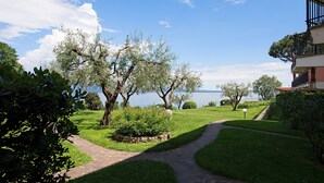 A pathway leading to a body of water with trees and a building in the background. - San Sivino Apartment with pool by Wonderful Italy (Manerba del Garda)