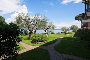 Un sentiero conduce a uno specchio d'acqua, sullo sfondo alberi e un edificio.