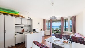 A compact kitchen with a dining area, a sofa, and a view of the sea. - San Sivino Apartment with pool by Wonderful Italy (Manerba del Garda)