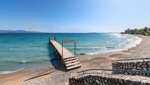 A wooden pier extending into calm waters, a stone wall, and a clear sky. - San Sivino Apartment with pool by Wonderful Italy (Manerba del Garda)