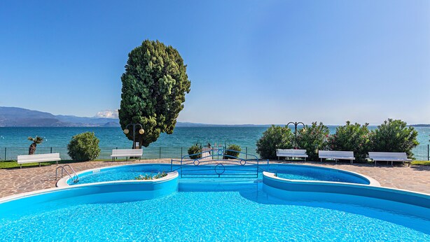 A swimming pool with a view of the sea, surrounded by benches and a tree. - San Sivino Apartment with pool by Wonderful Italy (Manerba del Garda)