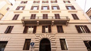 A multi-story building with a central entrance, multiple windows with shutters, and a balcony with a railing. - The Best Rent - Apartment in Piazza Venezia (Roma)