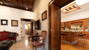 A spacious living area with a red sofa, a wooden dining table, and a kitchen with wooden cabinets and a bar. - The Best Rent - Apartment in Piazza Venezia (Roma)