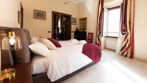 A bedroom with a large bed, a desk with a lamp, and a view of a window with curtains. - The Best Rent - Apartment in Piazza Venezia (Roma)