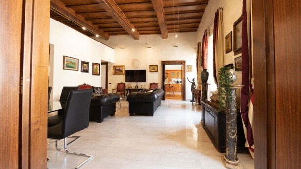 A spacious living area with a high ceiling, wooden beams, a black leather sofa, a glass coffee table, and a marble floor. - The Best Rent - Apartment in Piazza Venezia (Roma)