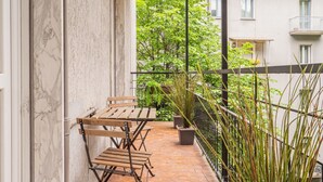 A balcony with wooden chairs and a table, potted plants, and a view of a tree-lined street. - The Best Rent - Apartment in Milan downtown (Milano)