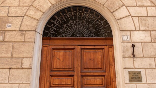 A double wooden door with a decorative metal grille above it, set in a stone wall. - The Best Rent - Apartment near Isola Tiberina (Roma)