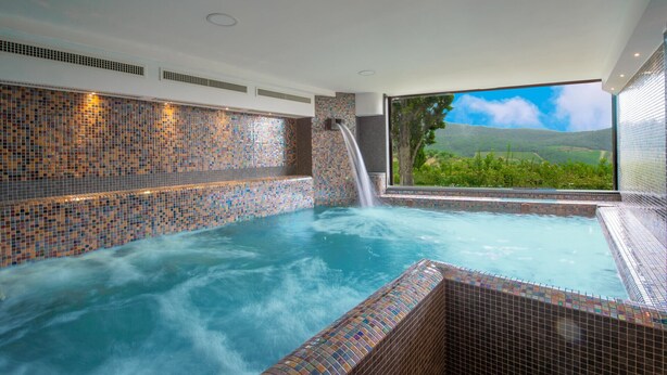 Un bain à remous aux parois recouvertes de mosaïques et agrémenté d’une cascade, le tout offrant une vue panoramique sur le paysage extérieur.