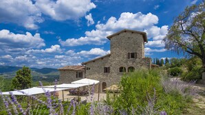 Un bâtiment en pierre doté d’une terrasse et de sièges en plein air, entouré de champs de lavande et surplombé par un paysage montagneux.