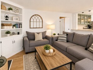 A living room with two grey sofas, a wooden coffee table, a white shelving unit, and a lamp.