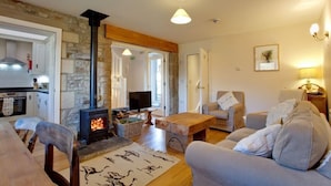 A cozy living room with a stone wall, a fireplace, a television, and comfortable seating. - Nethergill Haylofts (Skipton)