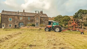 A stone house with a large field in front, a tractor, and a piece of farming equipment. - Nethergill Haylofts (Skipton)