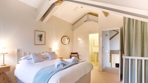 A bedroom with a large bed, bedside tables, a mirror, and a view of the bathroom. - Nethergill Haylofts (Skipton)