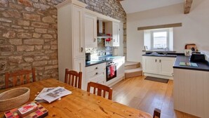 A kitchen with white cabinets, a stone wall, and a wooden dining table. - Nethergill Haylofts (Skipton)