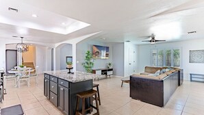 Amplia sala de estar con una isla central grande, un comedor con una mesa redonda y una zona de estar con sofá y banco.