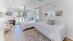 Un dormitorio moderno con dos camas, un ventilador de techo y un ventanal grande.