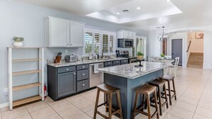 Una cocina moderna con armarios grises, una isla grande con taburetes y un comedor con candelabro.