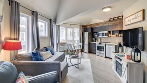 A modern living room with a sofa, a dining table, and a kitchen area with a microwave and oven. - Chouette Tremblant Ski In/Out Pedestrian Village (Mont Tremblant)