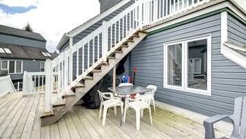 A wooden deck with a table and chairs, a staircase leading to a second floor, and a window with blinds.