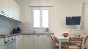 A compact kitchen with white cabinets, a built-in oven, a window above the sink, and a dining area with a table and chairs. - Modern 2bedroom apartment in the heart of Naxos, walking distance to the beach (Naxos)