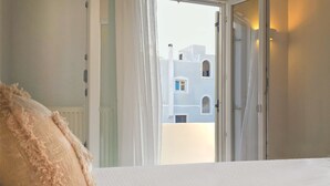 A hotel room with a bed, a view of buildings through an open door, and a window with curtains. - Modern 2bedroom apartment in the heart of Naxos, walking distance to the beach (Naxos)